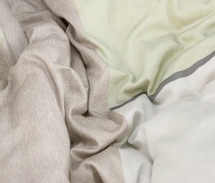 Nahaufnahme von zerknitterter Bettwäsche mit hellgrünen, gemusterten beigen und weißen Stoffabschnitten, getrennt durch einen dünnen dunkelgrauen Streifen.