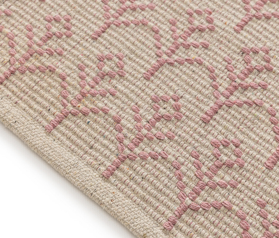 Detailaufnahme eines beigen Teppichs mit rosa geometrischem Muster.