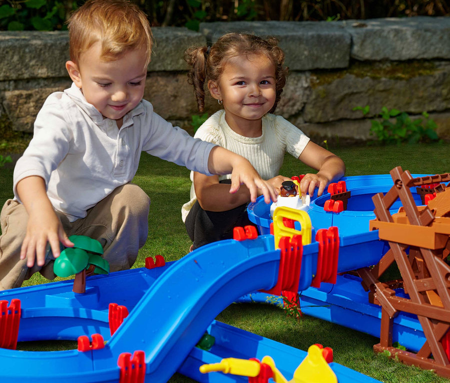 Zwei Kinder spielen mit der blauen AquaPlay Wasserbahn »WaterWheel« im Garten.