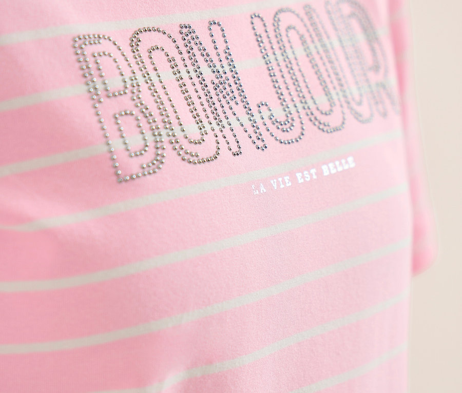 Nahaufnahme eines rosa-weiß gestreiften CECIL Shirts mit „BONJOUR“ aus silbernen Nieten und „LA VIE EST BELLE“ darunter.