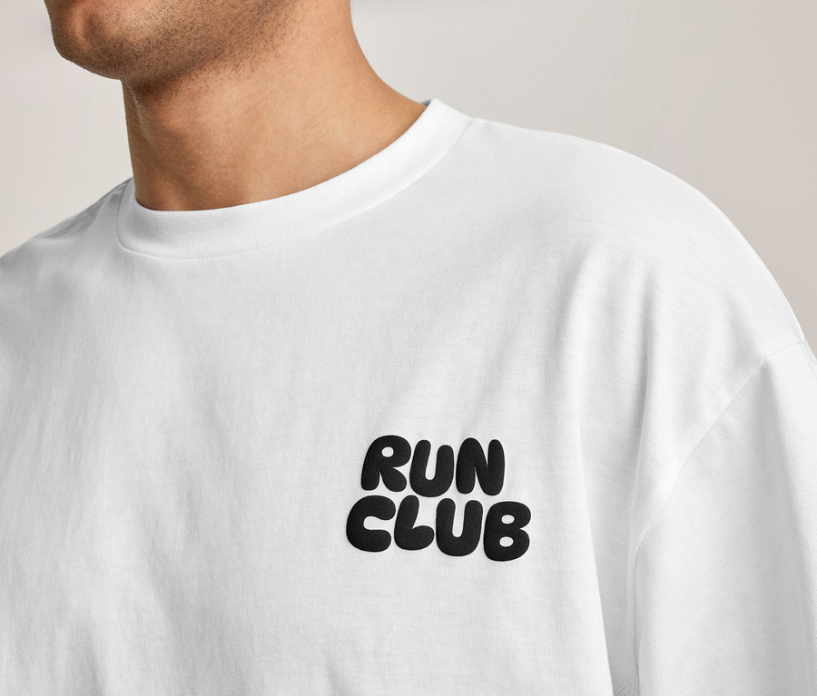 Eine Person trägt ein weißes Sportshirt mit der Aufschrift „RUN CLUB“ auf der Brust.