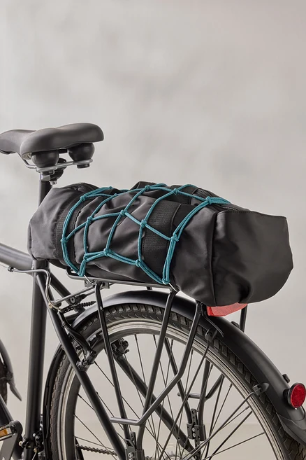 Eine schwarze Fahrradtasche ist mit einem blauen Gepäcknetz auf einem schwarzen Fahrradgepäckträger befestigt.