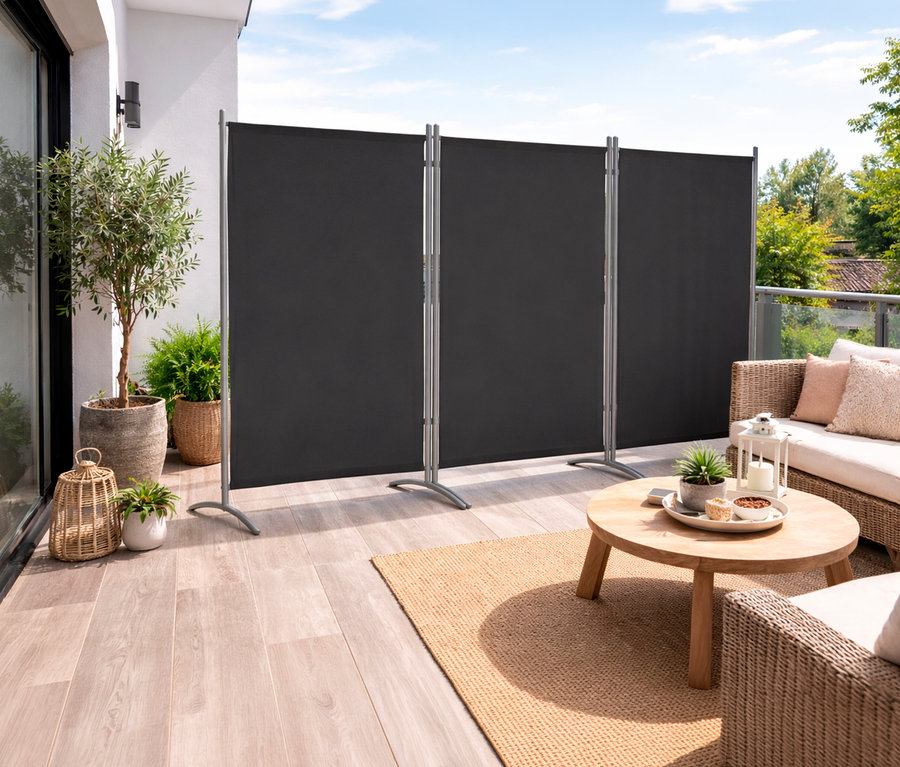 Auf einer Terrasse steht eine anthrazitfarbene, 3-teilige Leco Stellwand. Davor sind ein Tisch, ein Sofa und Pflanzen zu sehen.