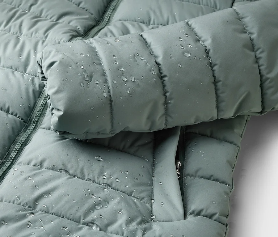 Nahaufnahme einer wasserabweisenden, gesteppten, hellgrünen Jacke mit Reißverschluss und Tropfen.