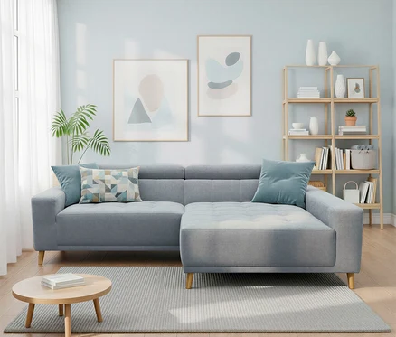 Ein hellblaues Wohnzimmer mit einem L-förmigen Sofa, einem runden Couchtisch auf einem grauen Teppich und einem Holzregal mit Büchern und Vasen. An der Wand hängen zwei abstrakte Bilder.
