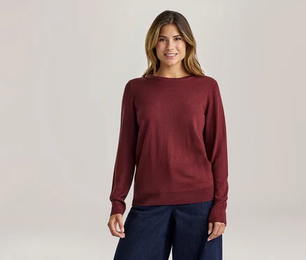 Lächelnde Frau in einem roten Langarmpullover und dunkelblauen weiten Hosen.