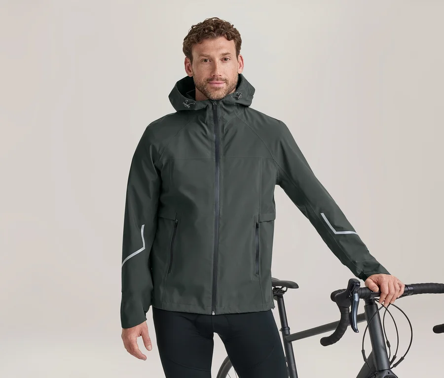 Mann in dunkelgrüner Kapuzenjacke mit reflektierenden Streifen, der neben einem Fahrrad steht und den Lenker hält.