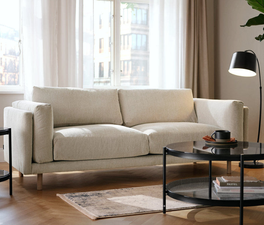 Beiges 2,5-Sitzer-Sofa, runder Glas-Beistelltisch, runder Glas-Couchtisch und schwarze Metall-Stehleuchte in einem Wohnzimmer mit Teppichen.