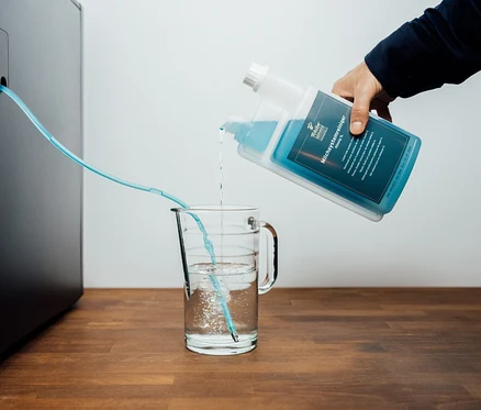 Person gießt flüssigen Reiniger in ein Glas, ein Schlauch führt zum Kaffeevollautomaten.