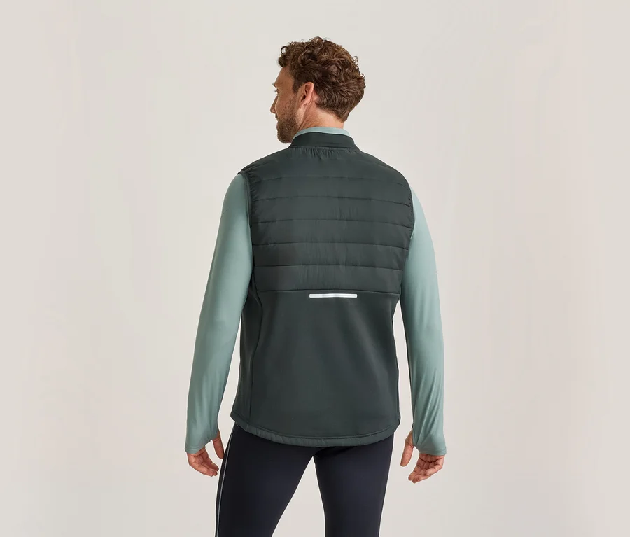 Mann von hinten, trägt eine dunkelgrüne Steppweste über einem hellgrünen Langarmshirt und dunklen Hosen. Die Weste hat einen reflektierenden Streifen am Rücken.