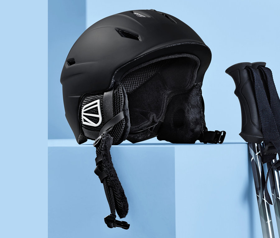 Schwarzer In-Mould-Ski- und Snowboardhelm und Skistöcke auf blauem Hintergrund.