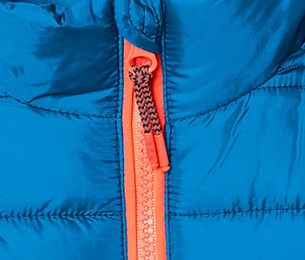 Detail einer blauen Steppjacke mit Farbverlauf und orangefarbenem Reißverschluss.