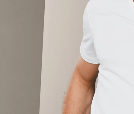 Mann lehnt an einer Wand und trägt ein weißes V-Ausschnitt-T-Shirt und karierte Boxershorts. Er trägt 2 Modal-Unterhemden.
