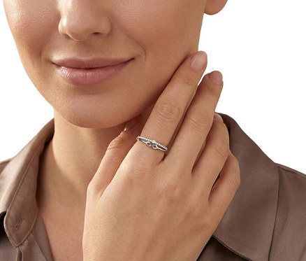 Nahaufnahme einer Frau, die einen Amor Ring mit Infinity-Symbol und kleinen Steinen am Ringfinger trägt. Ihre Hand berührt ihr Kinn.