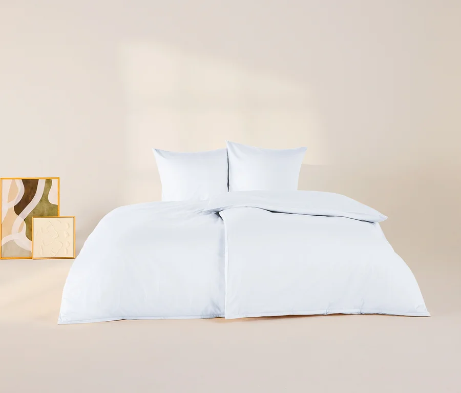 Weisse Baumwollsatin-Bettwäsche mit zwei Kissen und einer Bettdecke auf einem Bett, daneben zwei gerahmte abstrakte Kunstwerke.