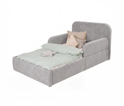 Ein graues Kindersofa-Bett aus weichem, strukturiertem Stoff, ausgezogen zu einem Bett. Es hat eine hellgrüne Bettdecke mit Punktmuster, mehrere beigefarbene Kissen und ein kleines sternförmiges Kissen.