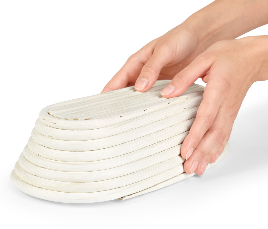 Zwei Hände halten ein ovales Gärkörbchen.