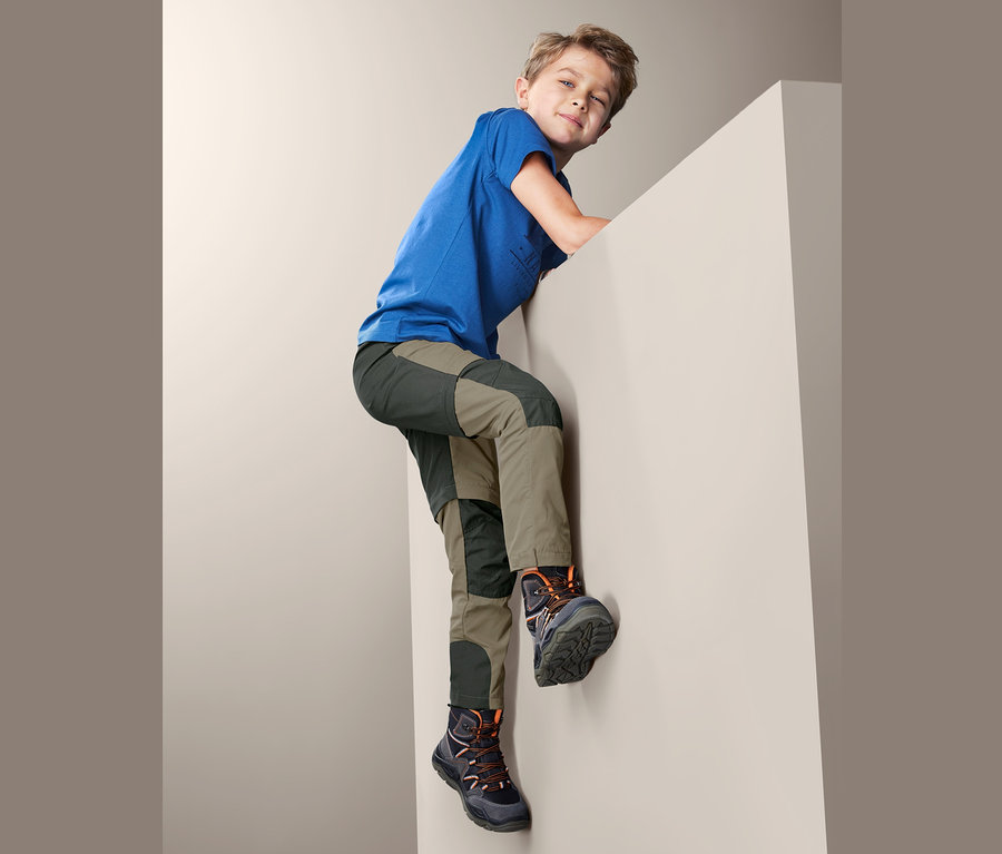 Junge in blauem T-Shirt und 2-in-1-Funktionshose klettert an einer Wand.