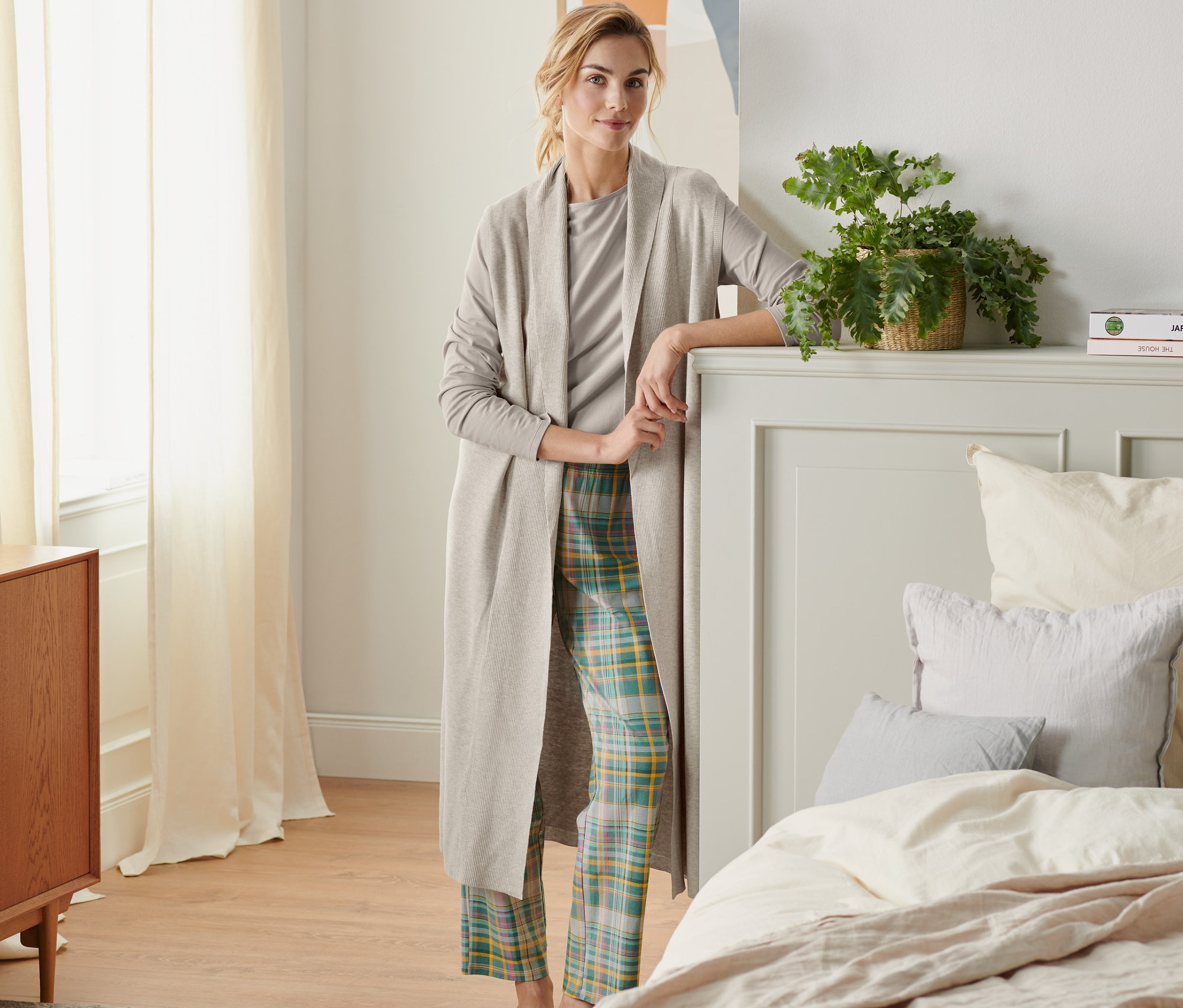 Frau steht im Schlafzimmer und trägt eine Loungeweste aus Strick.