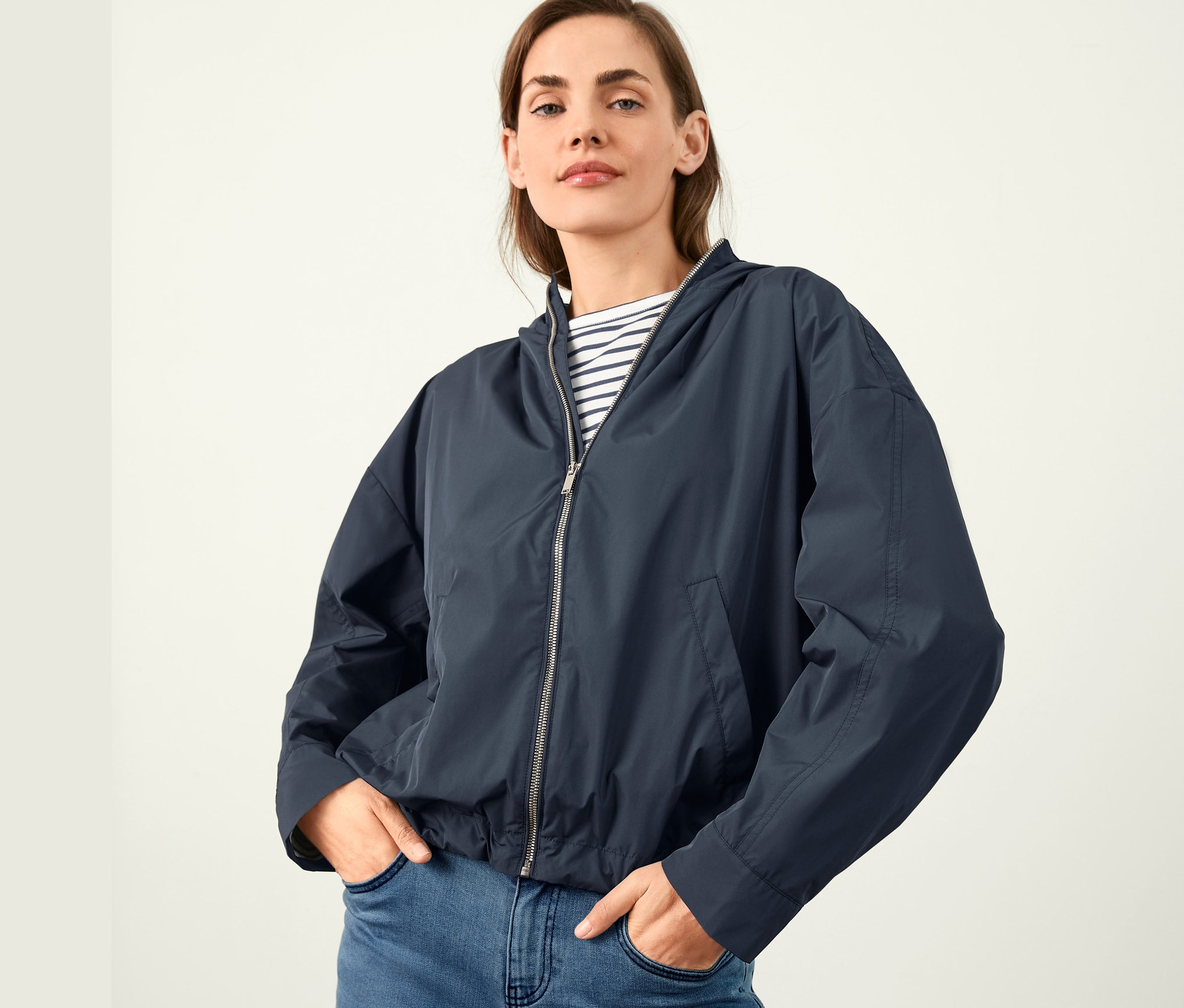 Frau posiert in kurzem Parka mit Kapuze und blauen Jeans.