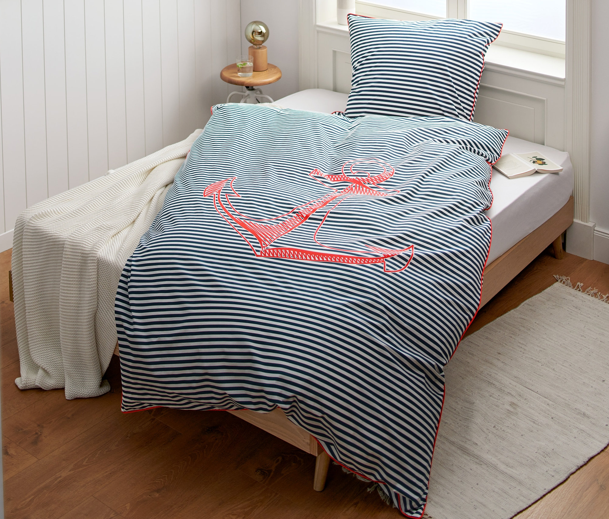 Renforcé-Bettwäsche Normalgröße mit blauen Streifen und rotem Anker auf einem Bett.