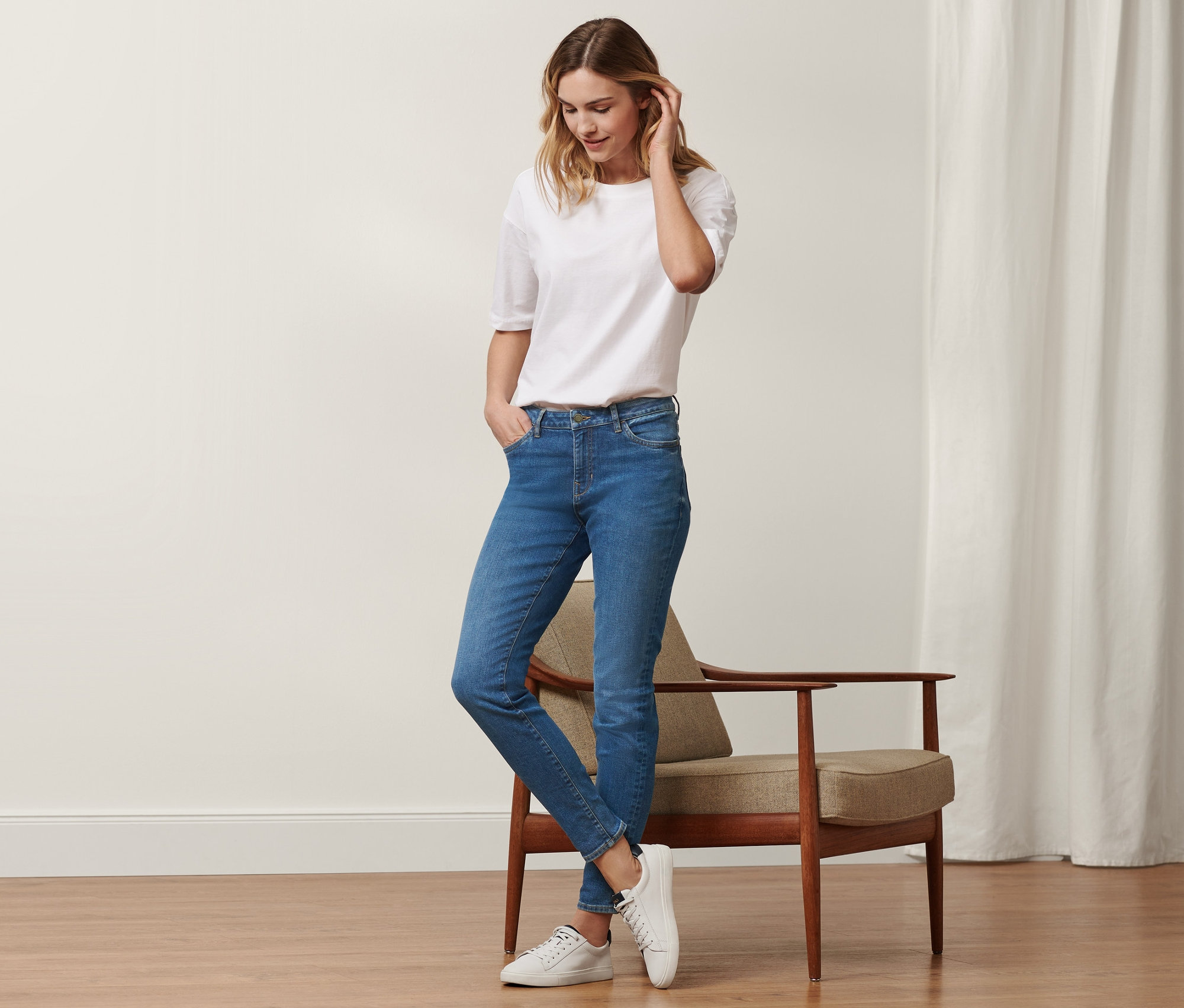 Eine Frau steht und trägt eine Slim-Denim »Fit Emma« in Mid Blue Denim und ein weißes T-Shirt.