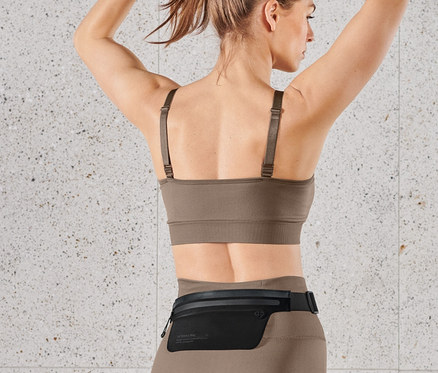 Frau bindet Haare zusammen und trägt Laufgürtel für Smartphones.