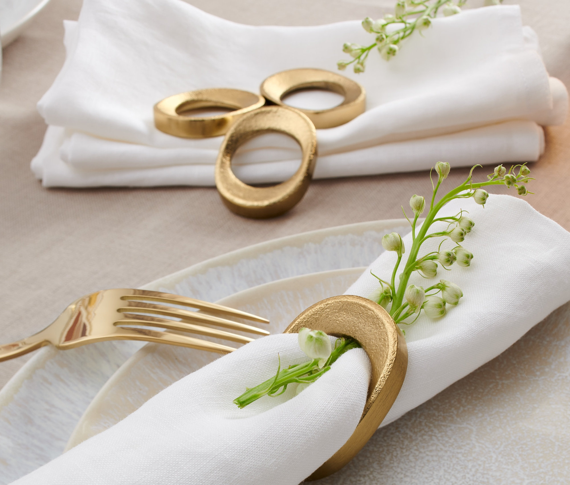 Weiße Servietten liegen mit 4 Serviettenringen auf einem Tisch.