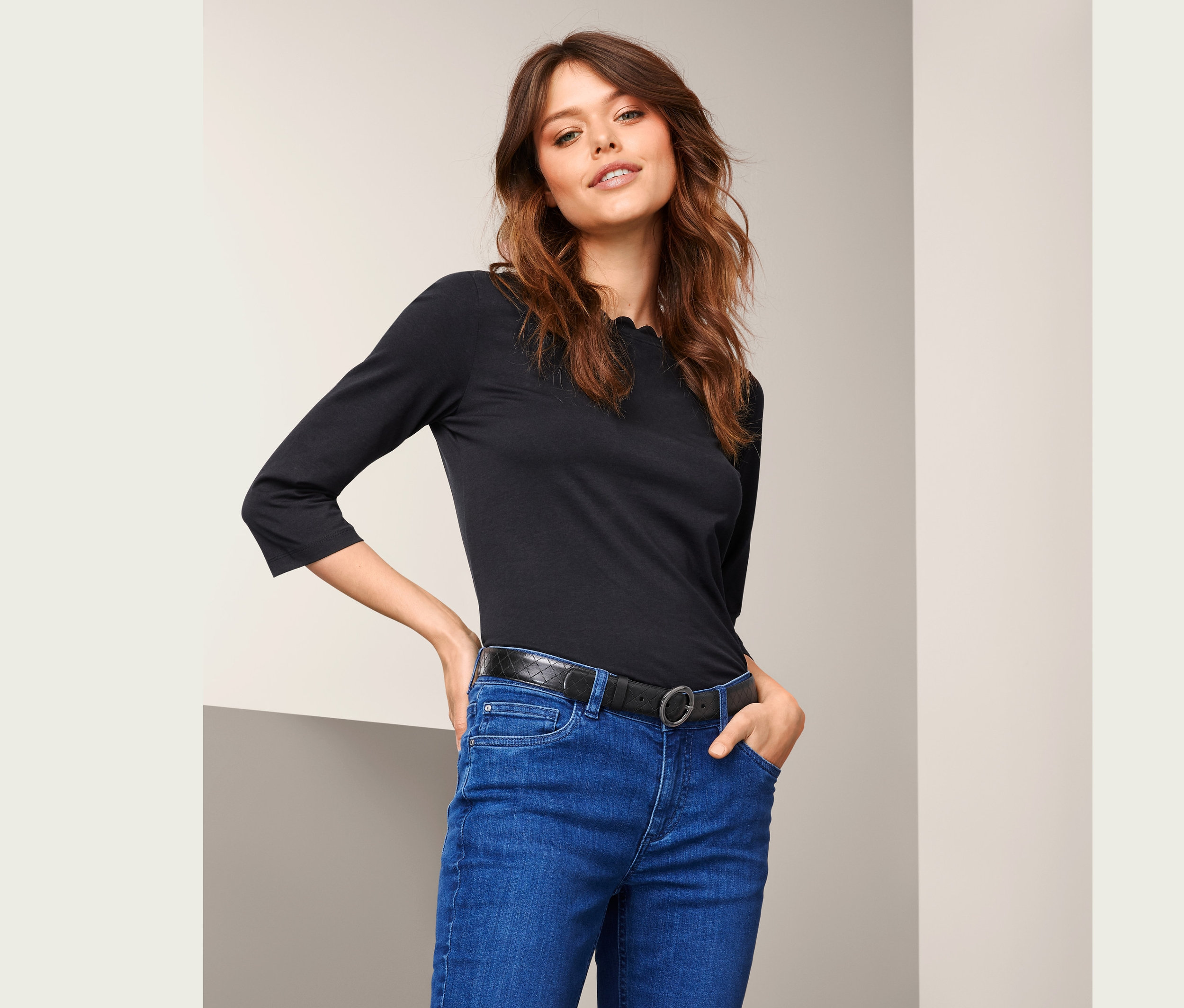 Frau posiert in blauen Jeans und schwarzem Oberteil mit Ledergürtel.