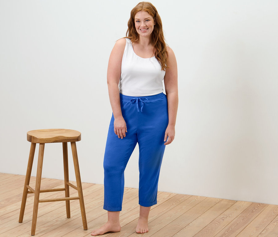 Frau steht und trägt ein weißes Hemdchen und eine blaue Pyjamahose.