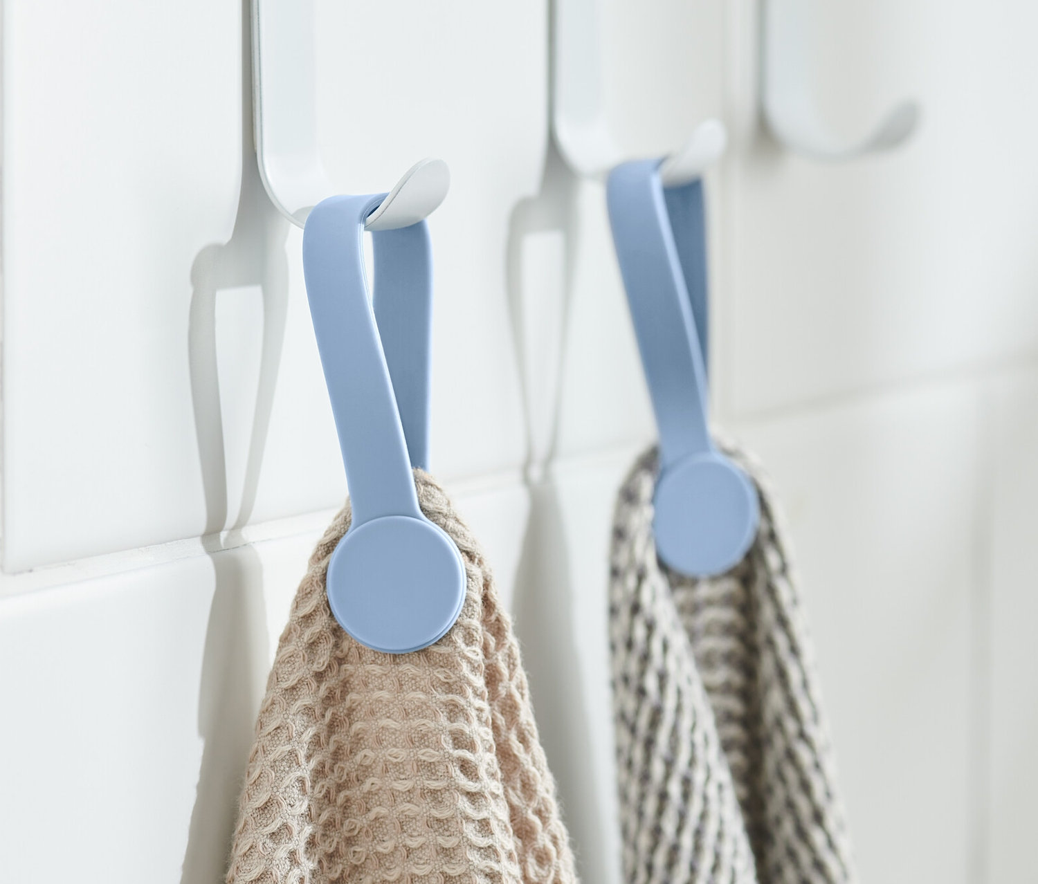 Zwei Handtücher hängen an weißen Haken mit 2 Magnet-Clips an einer weißen Wand.