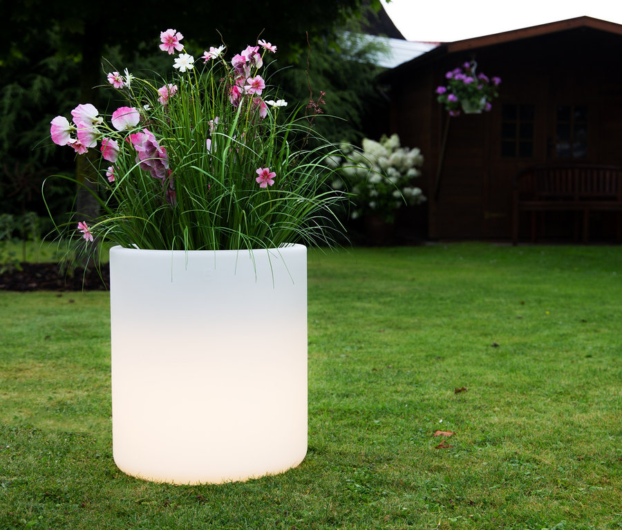 Blumen in einem weißen Blumentopf, im Hintergrund Rasen und ein Gartenhaus. 8 seasons design LED-Leuchte.