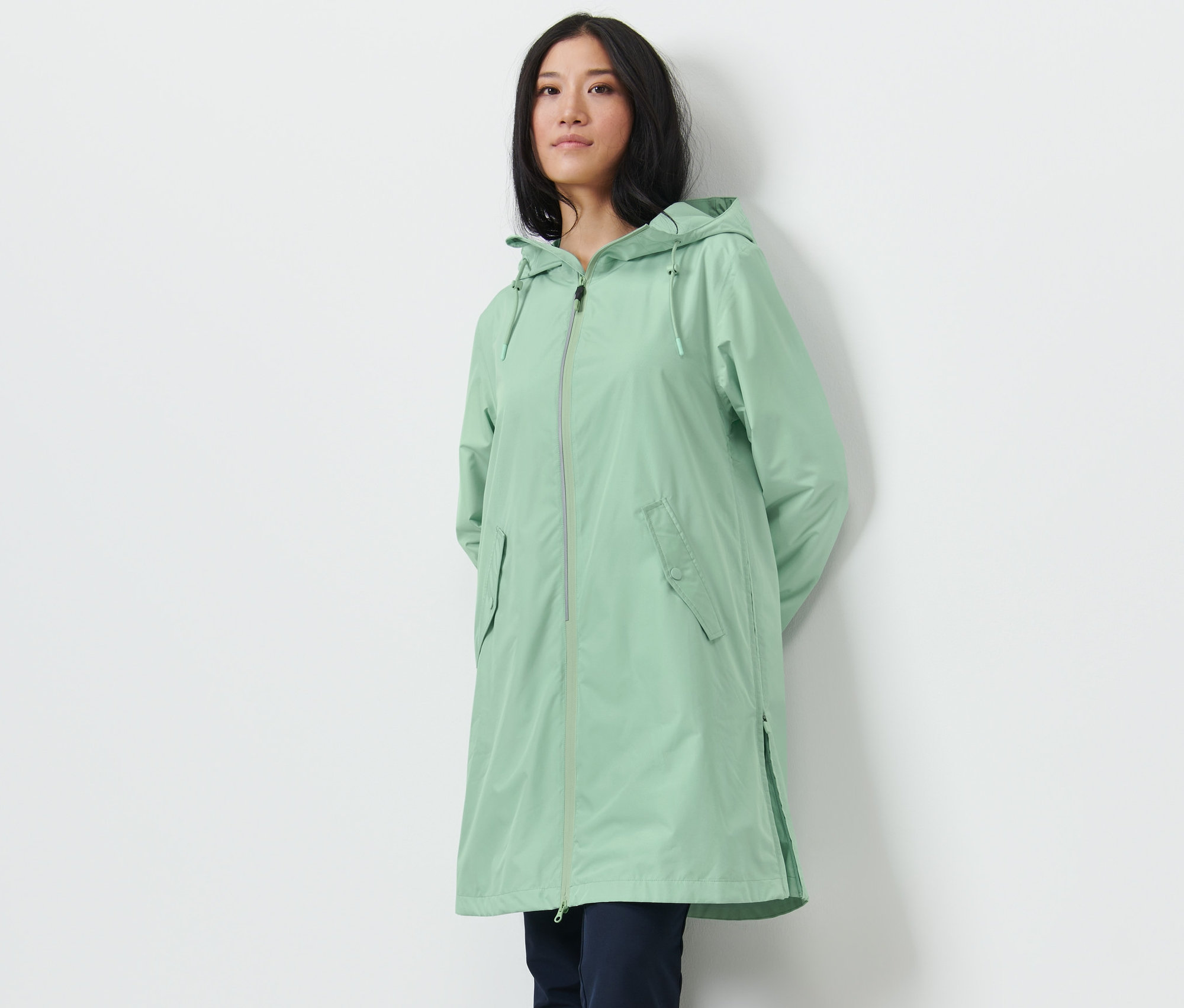 Eine Frau posiert in einem hellgrünen Regenmantel.