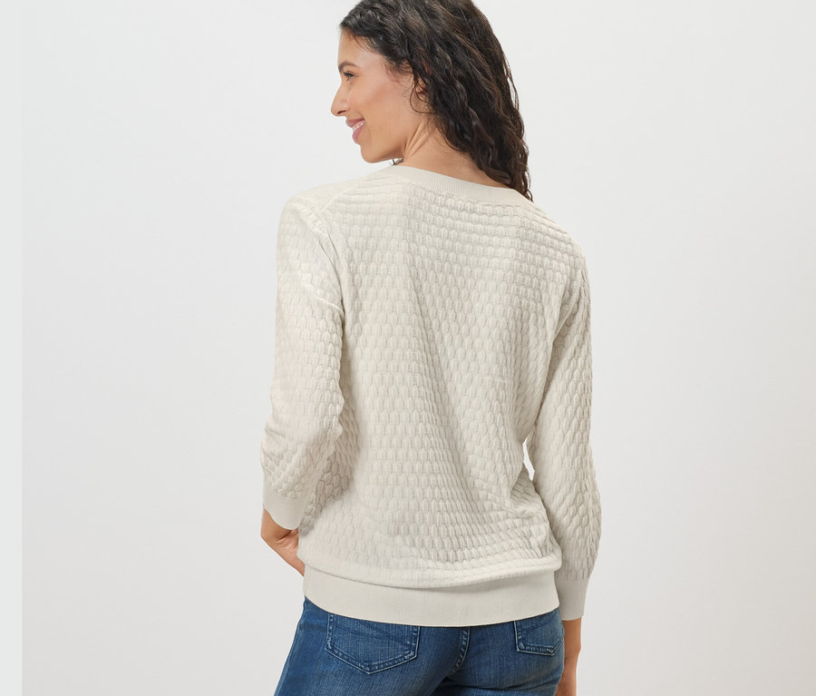 Frau schaut über die Schulter und trägt einen Strickpullover mit Struktur und Jeans.