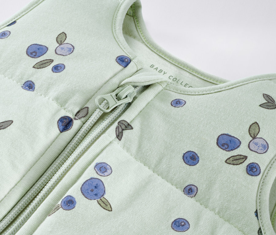 Detailaufnahme eines hellgrünen Schlafsacks mit Beerenmuster und Reißverschluss.