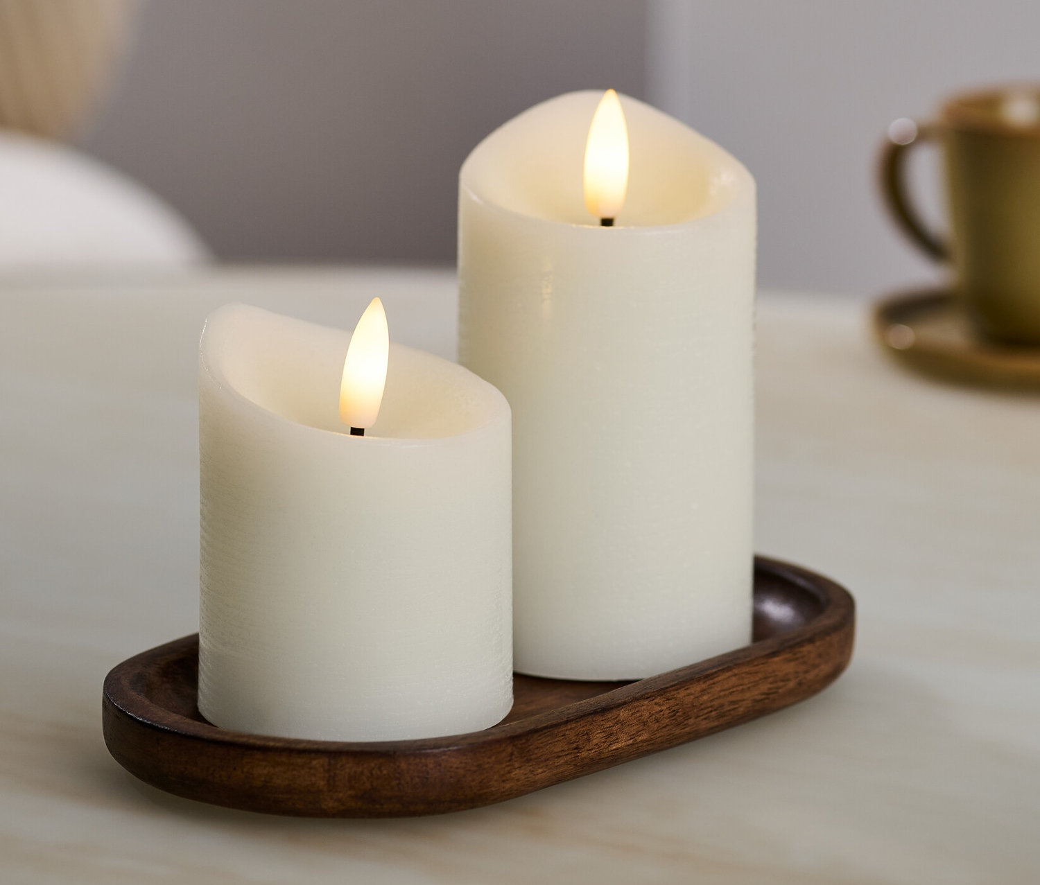 Zwei cremefarbene LED-Echtwachskerzen auf einem braunen Tablett.