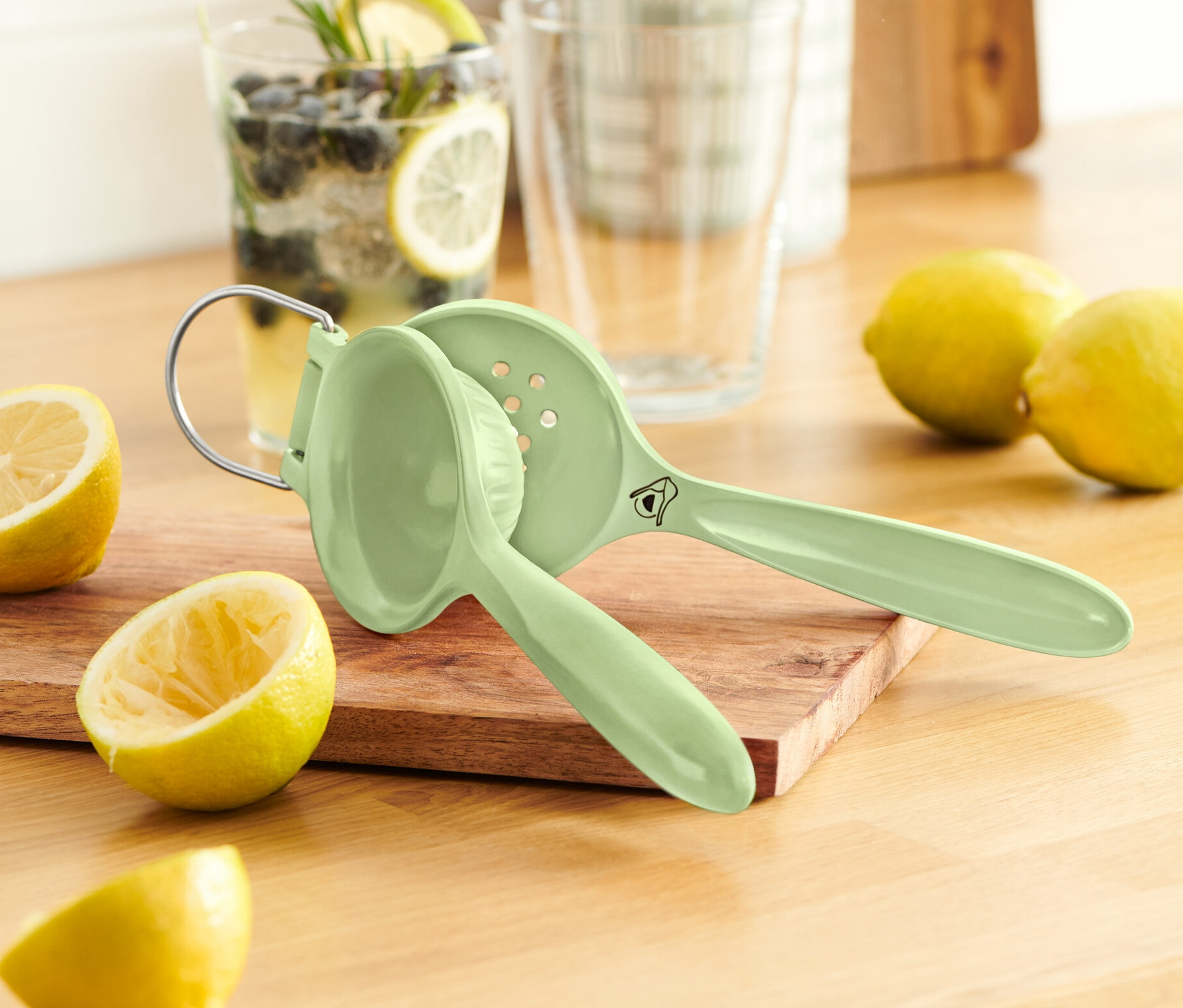 Eine grüne Zitruspresse liegt auf einem Holzbrett neben Zitronen.