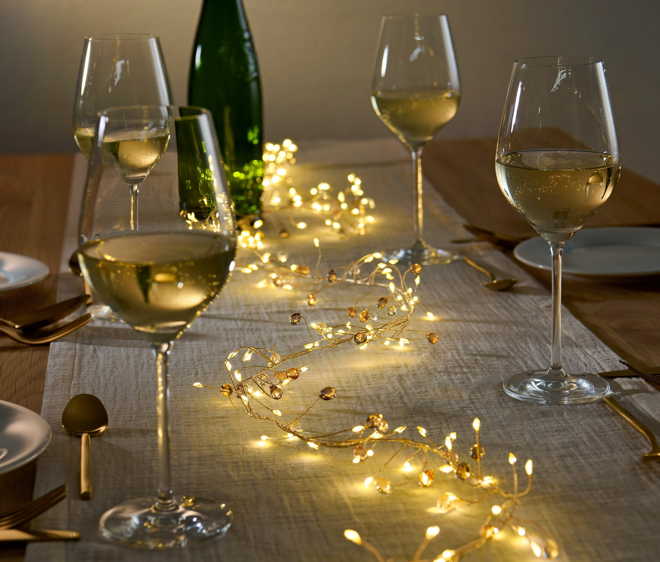 Gedeckter Tisch mit LED-Girlande, Weingläsern und Tellern.