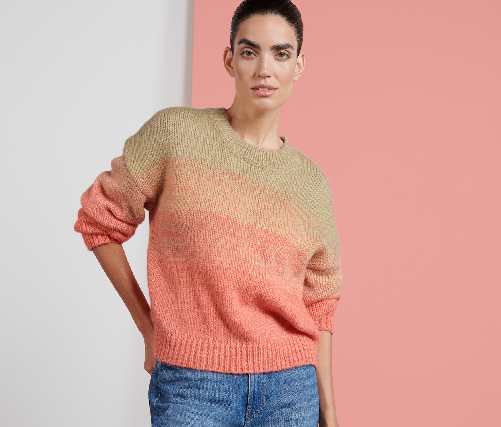 Eine Frau posiert in einem Grobstrick-Pullover und Jeans.