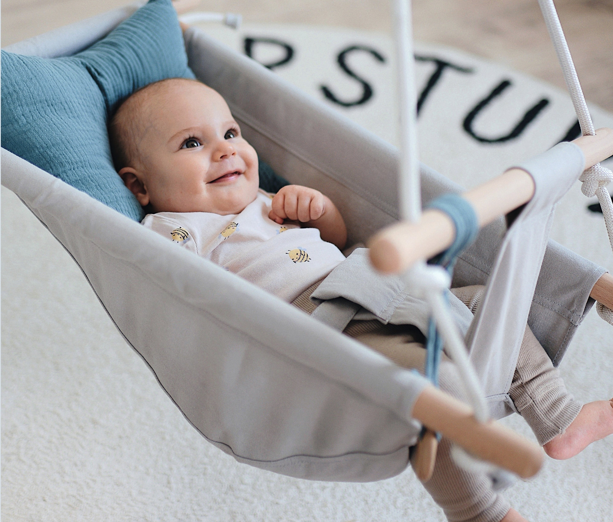 Lächelndes Baby liegt in grauer small foot Babyschaukel »Seaside« mit blauem Kissen.