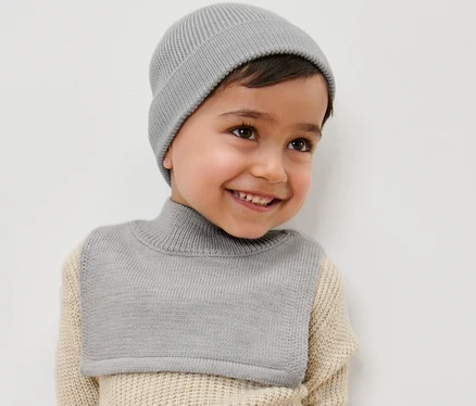 Ein lächelnder Junge trägt einen Kinder-Woll-Rollkragenschal und eine Mütze.
