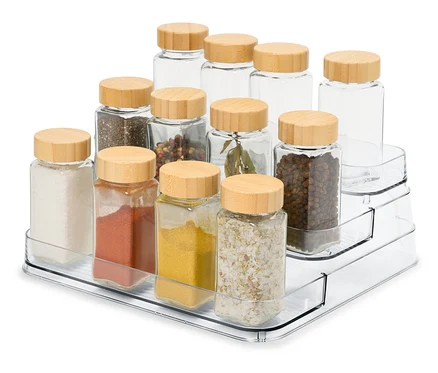 Auf einem durchsichtigen, dreistufigen Organizer befinden sich 12 Glas-Gewürzdosen mit Holzdeckeln.