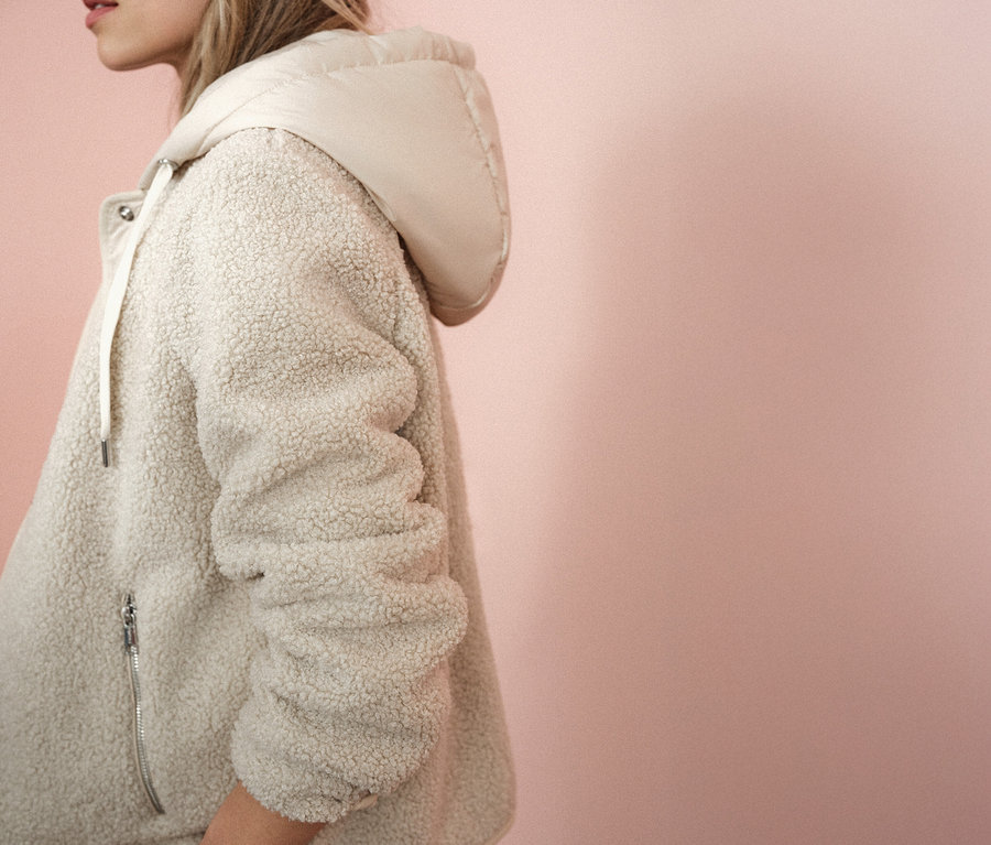 Frau trägt eine Street One Teddyjacke mit abnehmbarer Kapuze vor einem rosa Hintergrund.