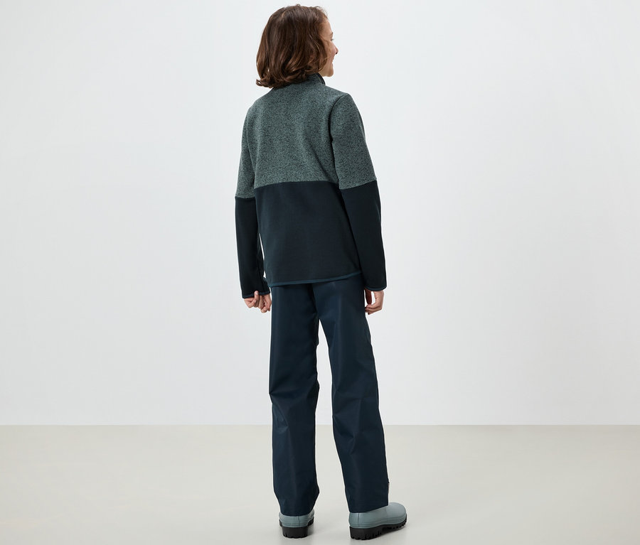 Ein Junge steht mit dem Rücken zur Kamera und trägt eine Kinder-Hybrid-Strickfleecejacke.
