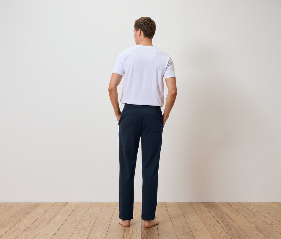 Mann mit dem Rücken zur Kamera trägt ein weißes T-Shirt und dunkelblaue Hosen.