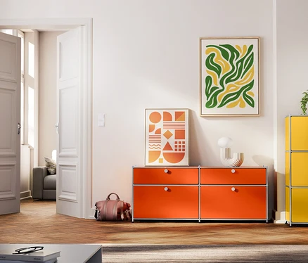 Wohnzimmer mit vier Metall-Möbeln: hellgraues Sideboard mit 2 Klappenfächern und 2 offenen Regalen, orangefarbenes Sideboard mit 2 Schubladen und 2 Klappenfächern, gelbe Kommode mit 3 Klappenfächern, grünes Sideboard mit 1 Klappenfach und offenem Regal.