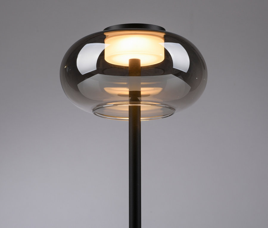 Stehlampe mit rauchfarbenem Glasschirm und schwarzem Fuß.