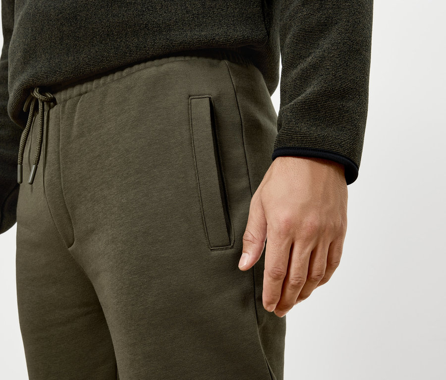 Mann trägt grüne Trainingshose und Pullover.