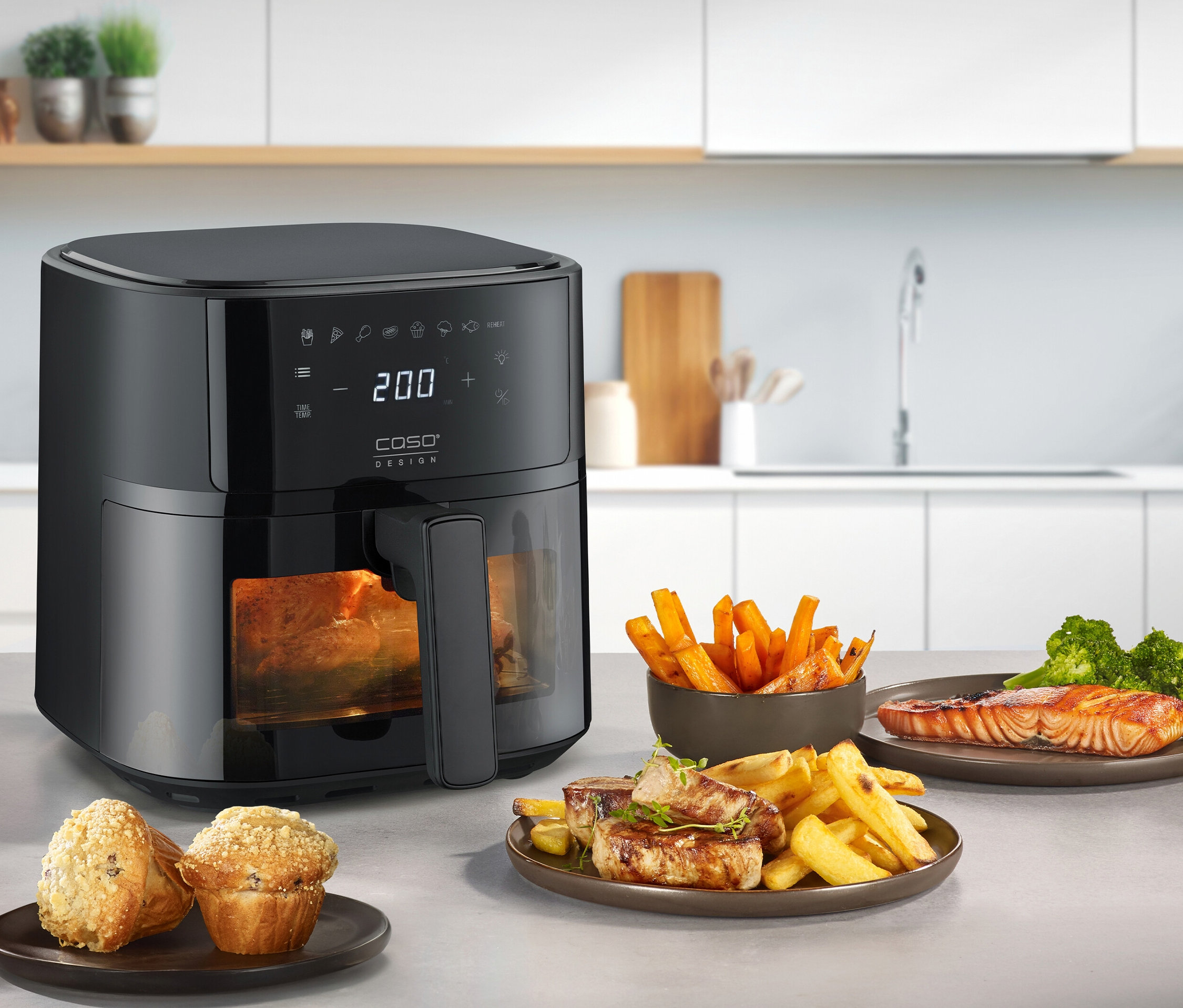 Eine schwarze CASO Heißluftfritteuse steht auf einer Küchentheke mit Speisen.