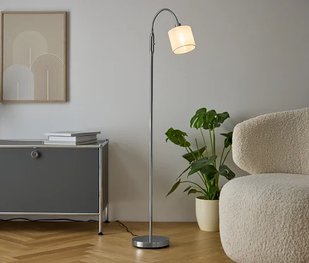 Innenraum mit grauer Kommode, Vase mit Trockenblumen, zwei Büchern, silberner Lampe und cremefarbenem Sessel.